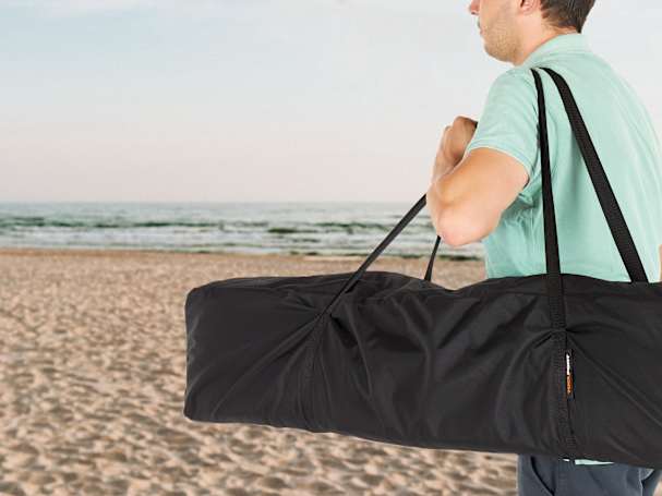 Hombre con carpa plegable en una bolsa en la playa