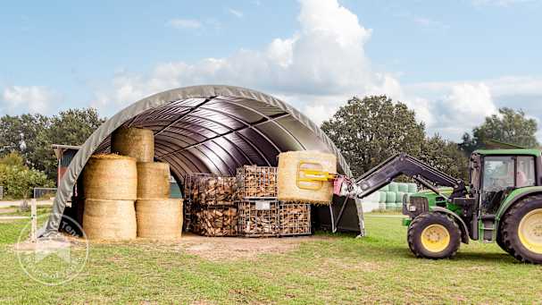 Arched shelter used for storing hay bales, firewood, and equipment with tractor loading hay