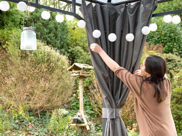 Woman fastening gazebo curtains on hardtop 4x4m garden gazebo